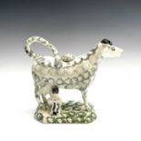 A pottery cow creamer, circa 1800, with sponged grey and puce decoration, the base with milkmaid and