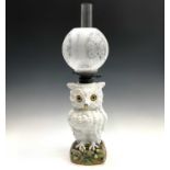 A large German porcelain owl oil lamp, late 19th century, with glass inset eyes, on an acorn moulded