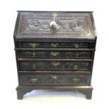 A George III carved oak bureau, the fall front carved with three portraits enclosing a fitted