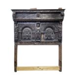 A carved oak bedhead, early 17th century, with central carved figure and masks amongst foliage,