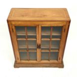 An Arts and crafts Cotswold school walnut glazed bookcase, the sycamore banded top with rounded