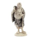 A Japanese Meiji period carved ivory netsuke depicting a standing Hotei Buddha carrying a sack,