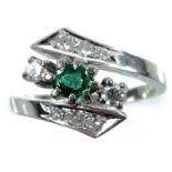 A 14ct white gold damond and emerald crossover nine stone ring, the oval cut emerald measuring 0.