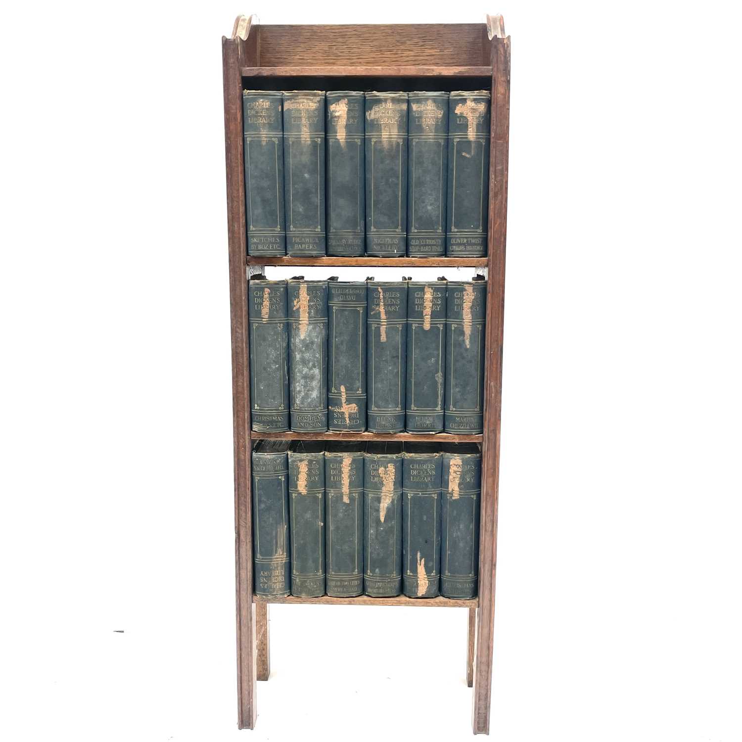 An oak narrow bookcase, early 20th century, containing 18 volumes of the Charles Dickens library,