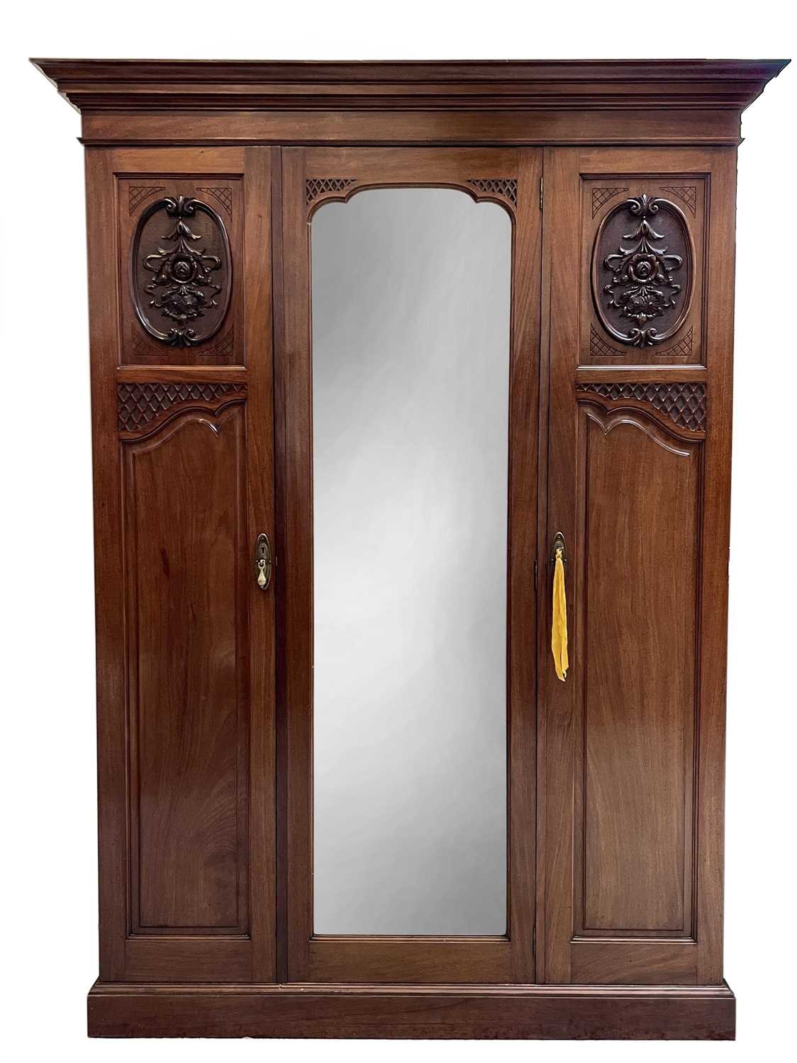 A late Victorian walnut triple wardrobe, with floral carved and mirrored panels enclosing hanging