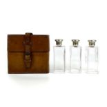 An Edwardian leather cased set of three spirit bottles with silver lids.