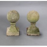 A pair of well weathered reconstituted stone circular garden gate post caps, raised on square