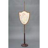 An Edwardian mahogany shield shaped pole screen with wool work banner depicting a beehive, raised on