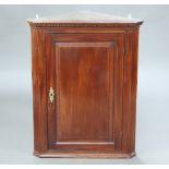 A Georgian mahogany hanging corner cabinet with moulded and dentilled cornice enclosed by a panelled