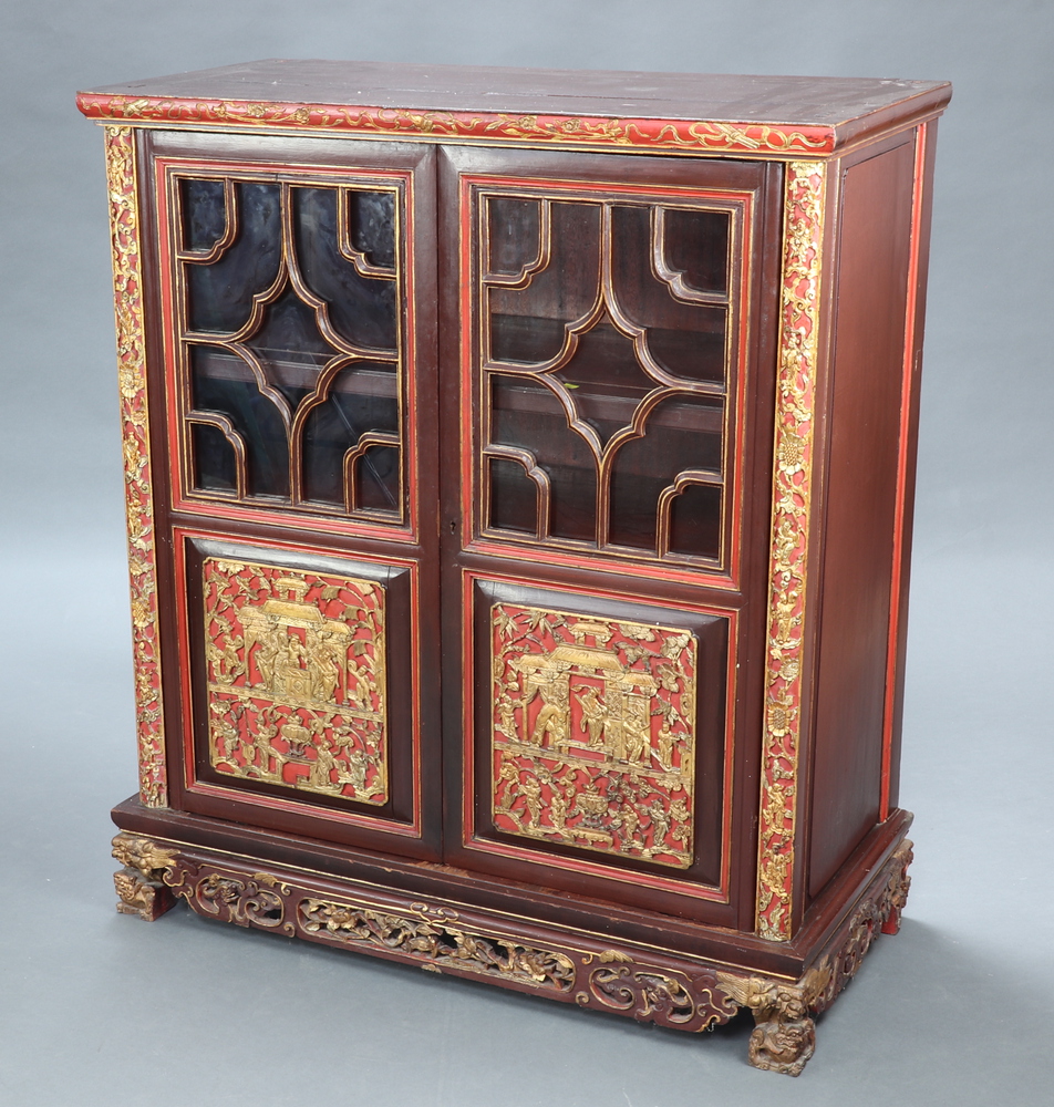A Chinese carved hardwood cabinet, fitted shelves enclosed by a pair of astragal glazed panelled