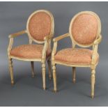 A pair of Empire style, carved beech, open arm salon chairs, raised on turned and reeded supports