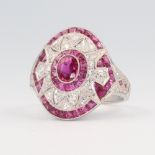 A white metal ruby and diamond cocktail ring, the centre oval cut ruby surrounded by tapered cut