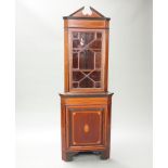 An Edwardian inlaid mahogany double corner cabinet with shaped cornice, fitted shelves enclosed by