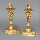 A pair of 19th/20th Century gilt metal candlesticks supported by cherubs and with lion mask