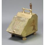 An Arts & Crafts embossed brass coal bin with hinged lid on shaped feet, complete with shovel,