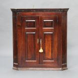 A Georgian oak hanging corner cabinet with moulded and dentil cornice enclosed by panelled doors