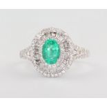 A white metal 14k oval emerald and diamond cluster ring, the centre stone 0.8ct the brilliant and