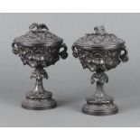 A pair of Victorian spelter lidded twin handled urns with leaf decoration, raised on circular