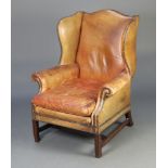 A Georgian style winged armchair upholstered in brown leather, raised on square supports 107cm h x