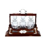 AN EDWARDIAN OAK THREE BOTTLE TANTALUS with silver-plated mounts containing three square half-cut