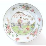 A Chinese famille rose plate decorated with a woman holding a fan in a garden terrace with a young