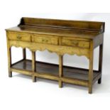 A late 18thC oak dresser base with a shaped upstand above three short drawers with brass handles and