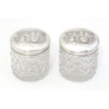 A pair of cut glass dressing table pots with embossed silver lids depicting angels after Sir