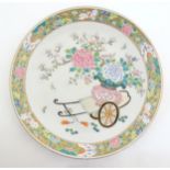 A Chinese famille rose charger depicting a cart carrying a vase of blossoming flowers, the border