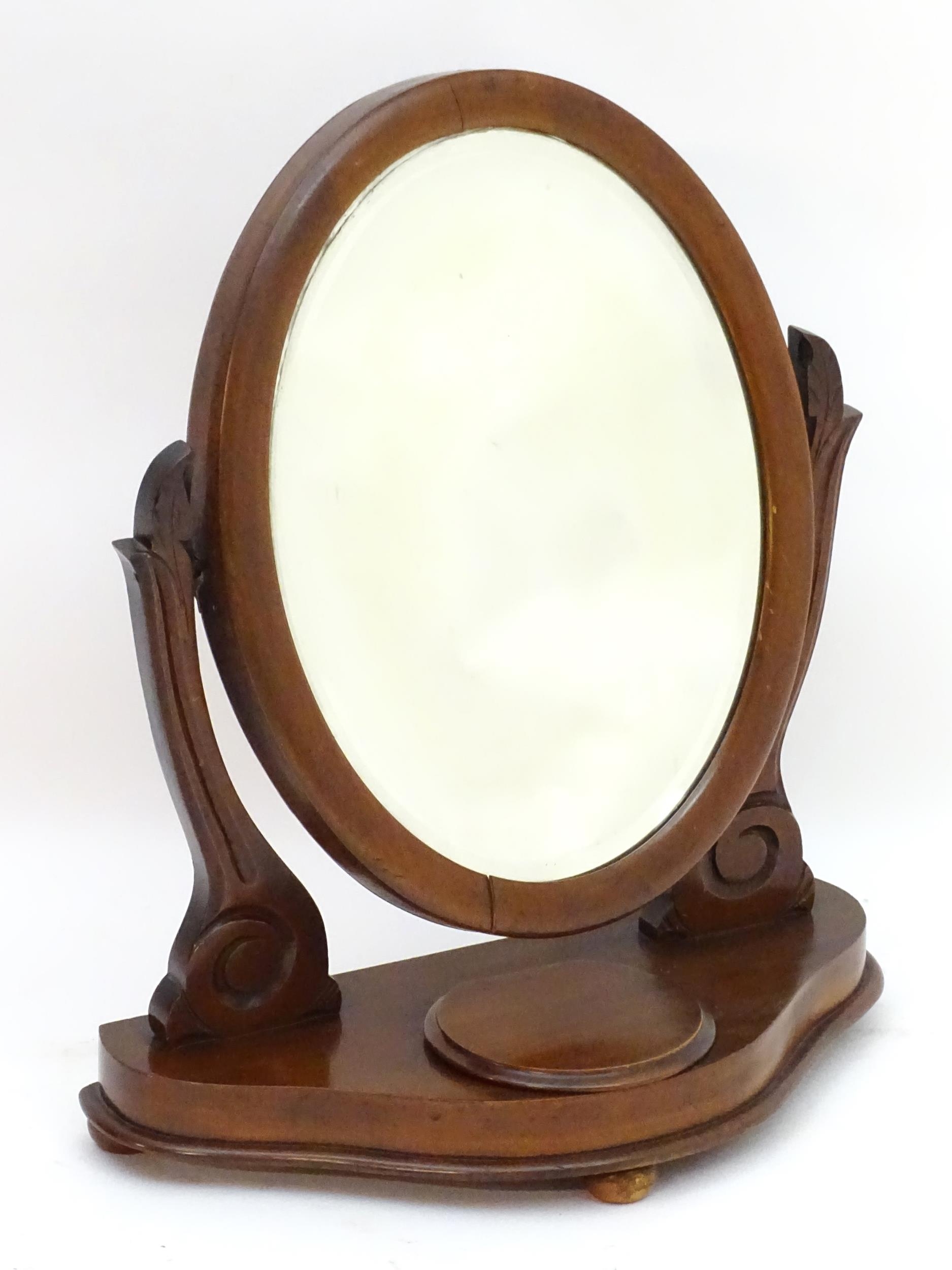 A Victorian mahogany toilet mirror with an oval mirror and shaped surrounds above a moulded base