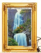 A backlit photograph of a waterfall with a mirrored background and a gilt frame. Approx. 26" x 18"