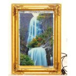 A backlit photograph of a waterfall with a mirrored background and a gilt frame. Approx. 26" x 18"