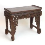 A 19thC Chinese lacquered table with raised ends and carved pierced fretwork decoration to the