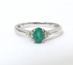 A 10ct white gold ring set with central emerald flanked by three diamonds each shoulder. Ring size