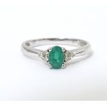 A 10ct white gold ring set with central emerald flanked by three diamonds each shoulder. Ring size