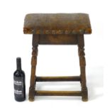 An early 20thC peg jointed oak stool with an embossed leather top and metal studs above a four