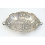 A Continental silver dish of lobed form with twin handles and embossed decoration. Indistinctly