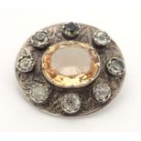 A white metal brooch set with central citrine bordered by white stones. 1" wide Please Note - we