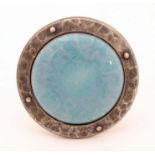 An Arts and Crafts white metal brooch of circular form set with central Ruskin style ceramic