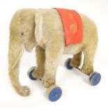 Toy: An early 20thC Steiff mohair pull along elephant toy with felt saddle, upon four wooden wheels,