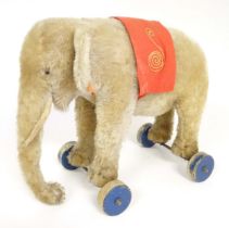 Toy: An early 20thC Steiff mohair pull along elephant toy with felt saddle, upon four wooden wheels,