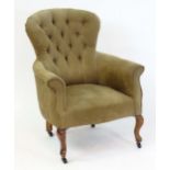 An early 20thC armchair with a deep buttoned back rest and a sprung seat above shaped legs