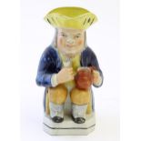 A Toby jug modelled as a seated man holding a beaker and a jug, with moulded caryatid handle.