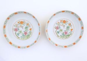 A pair of Chinese plates / dishes with central roundels depicting flowers and a foliate border.