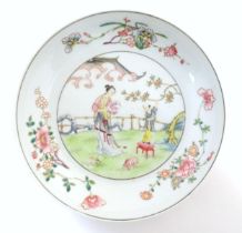 A Chinese famille rose plate decorated with a woman holding a fan in a garden terrace with a young
