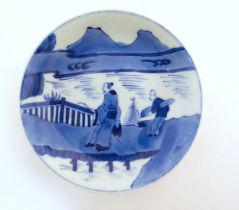 A Chinese blue and white dish with two figures crossing a bridge in a mountain landscape.