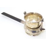 A silver tea strainer modelled as a stylised teapot with suspended strainer above, the base with