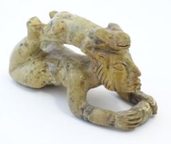 A 20thC soapstone model of a stylised figure lying on their front with a stylised rabbit / animal on