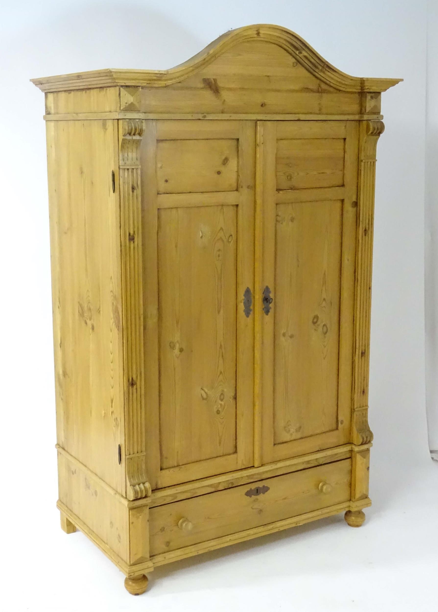 A 20thC continental pine wardrobe with an arched cornice above two panelled doors flanked by