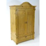 A 20thC continental pine wardrobe with an arched cornice above two panelled doors flanked by