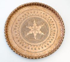 An early 20thC copper charger with scalloped edge, central Arts & Crafts style floral motif and